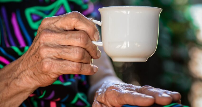 person holding white ceramic teacup to illustrate an older person in their own home
